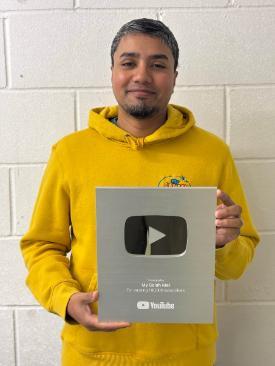 A man in a yellow jumper holds up a YouTube Play award