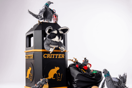 Sculpture of a rubbish bin with a stuffed raccoon inside, surrounded by stuffed pigeons and rubbish