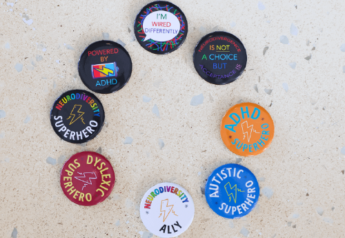 Pin badges arranged in a circle, with various slogans about neurodiversity on them