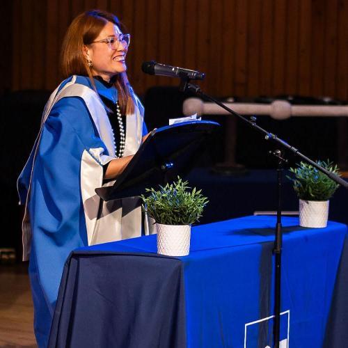 Ping Coombes gives a speech in a blue robe