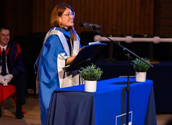 Ping Coombes gives a speech in a blue robe