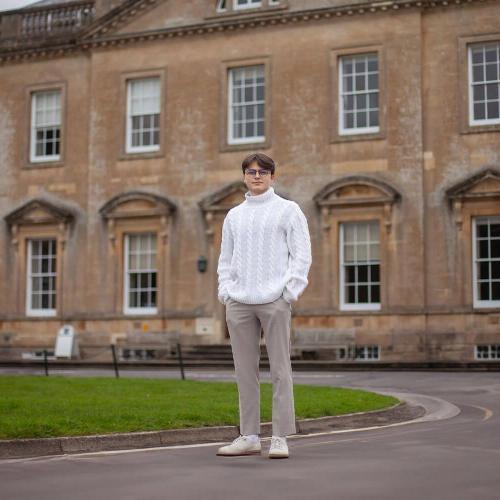 A man in a white turtleneck stands by BSU's Main House