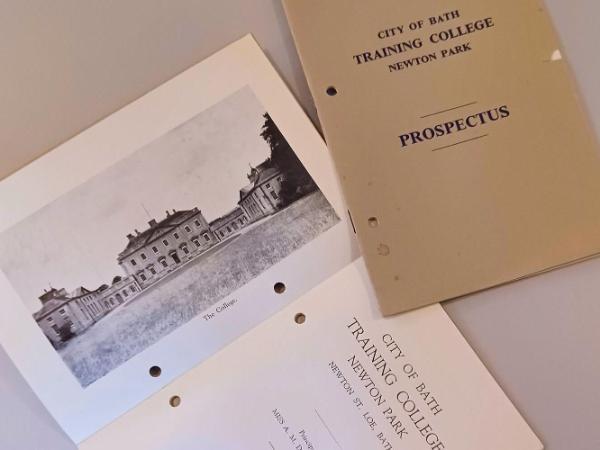 Papers on a table show a photo of Newton Park Main House, and the title page of Newton Park Training College's prospectus from 1948