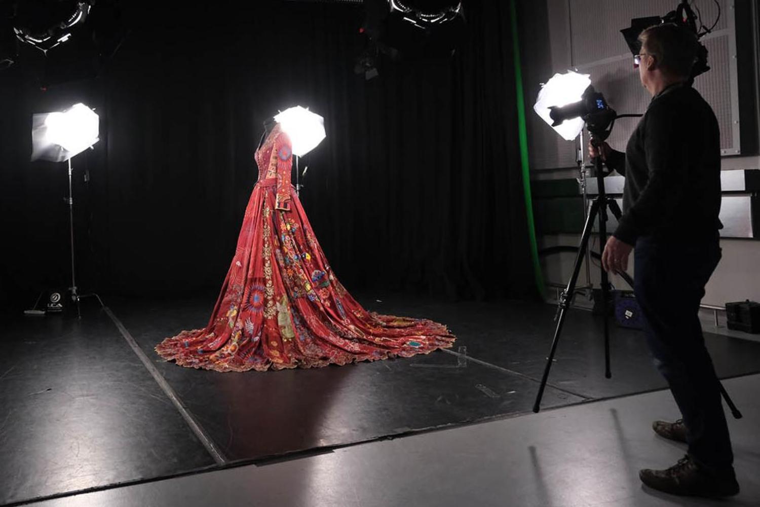 A beautiful, embroidered Red Dress on display in a studio with people taking photos of it