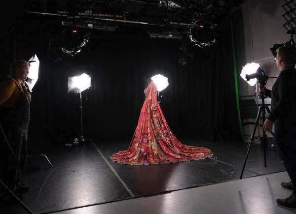 A beautiful, embroidered Red Dress on display in a studio with people taking photos of it