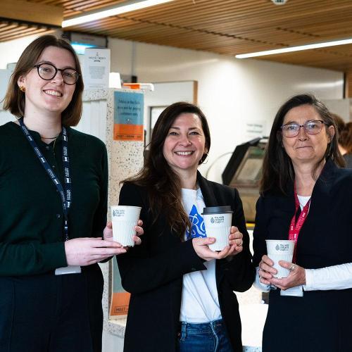 three women smile holding their reusable cups in front of a cafe counter