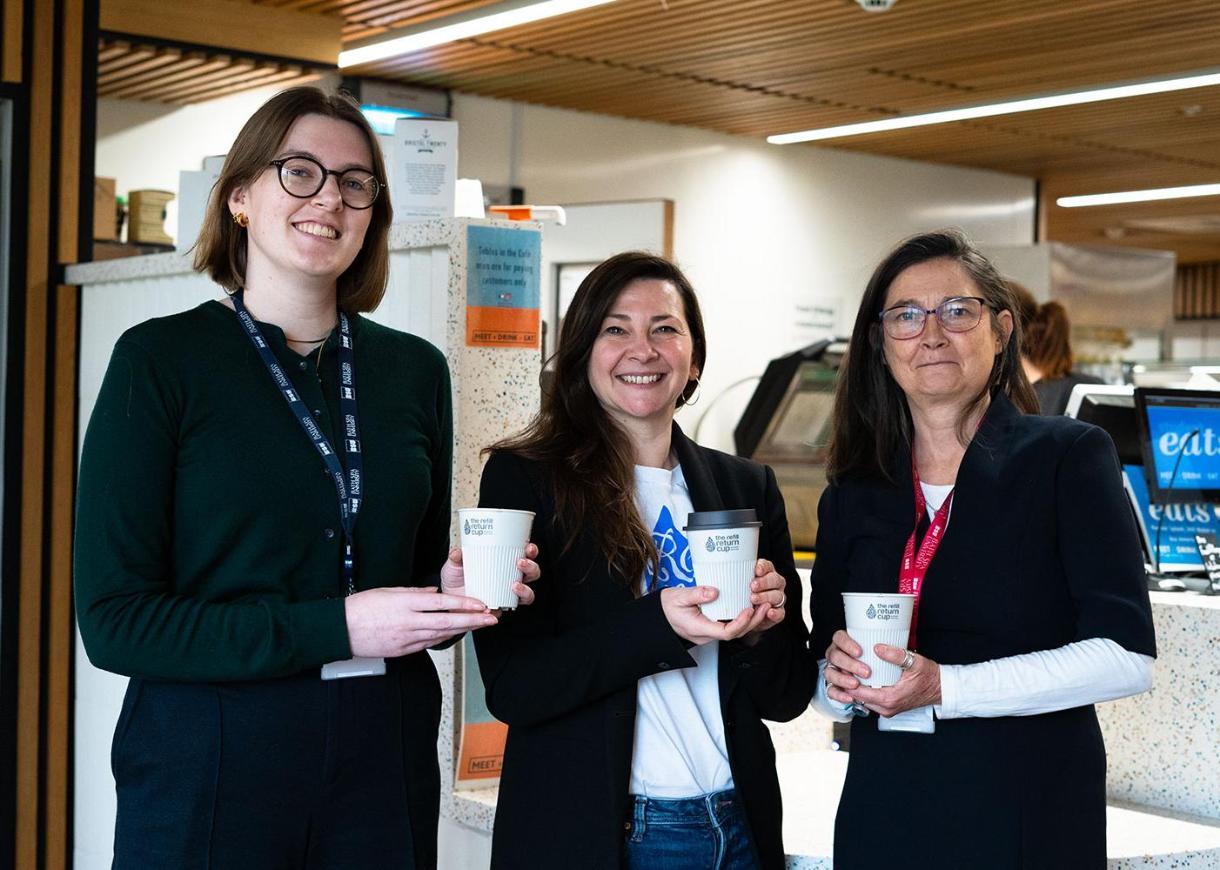 three women smile holding their reusable cups in front of a cafe counter