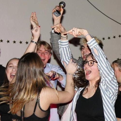 A group of young students celebrate winning by holding up a small silver glitterball trophy