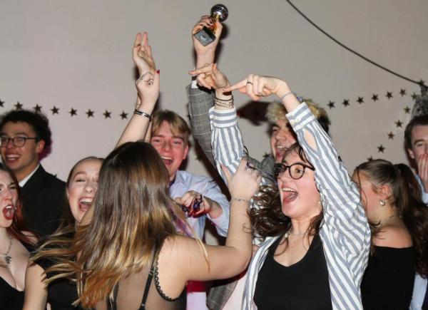 A group of young students celebrate winning by holding up a small silver glitterball trophy