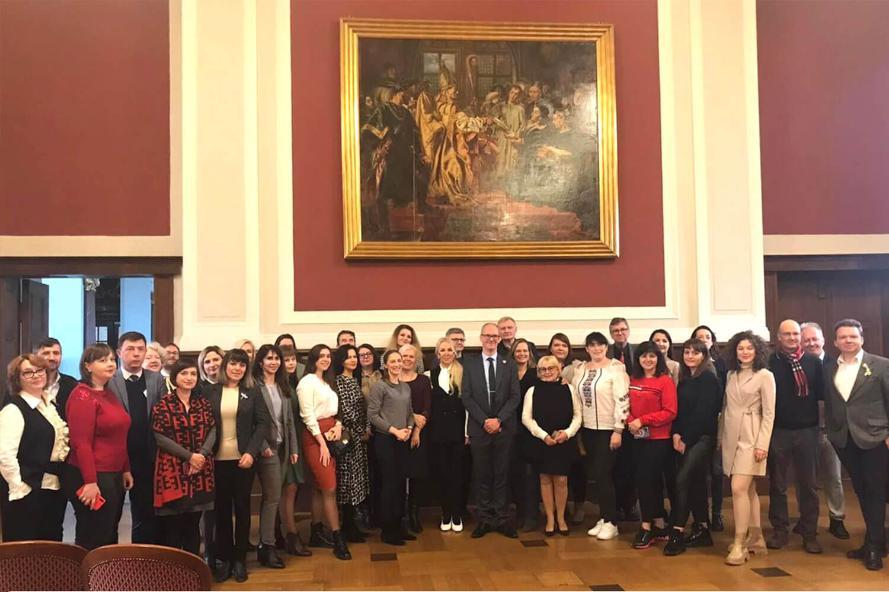 a group of people stand together in a larger room in front of a large painting.