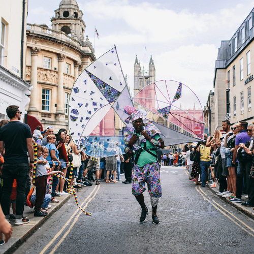 A man dressed in colourful clothing walks through the centre of Bath