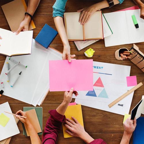 A top down image of people working, paper is scattered across the table