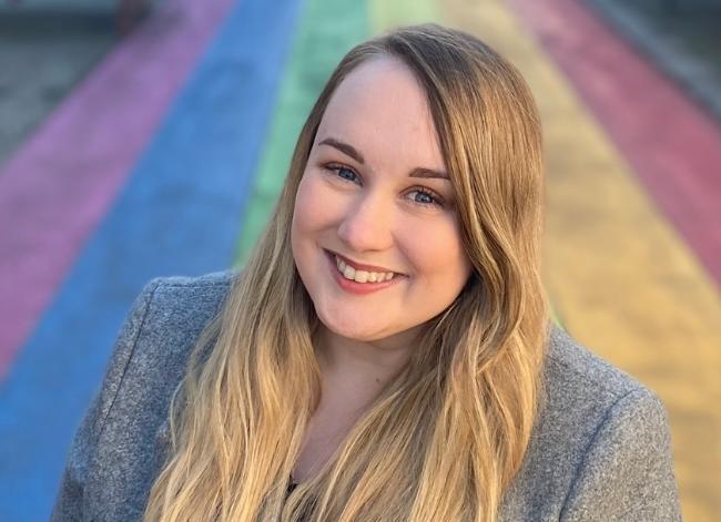 A person with long, blonde hair smiles at the camera