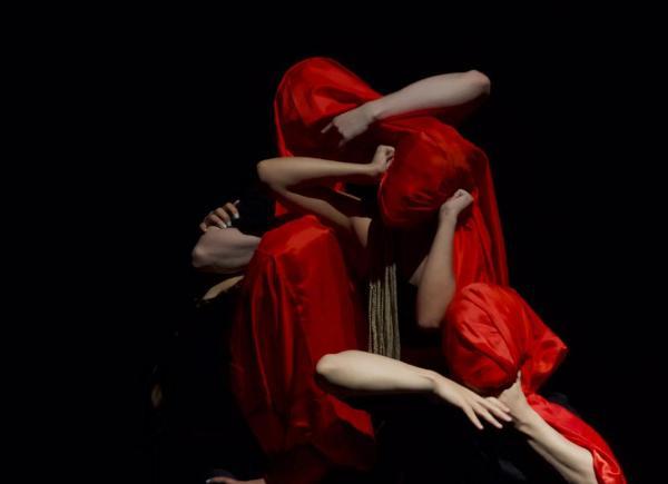 Dancers in red creating a shape on a dark stage