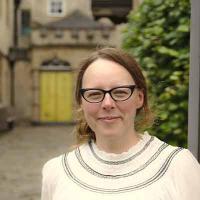 Person with shoulder length blonde hair wearing glasses and white jumper