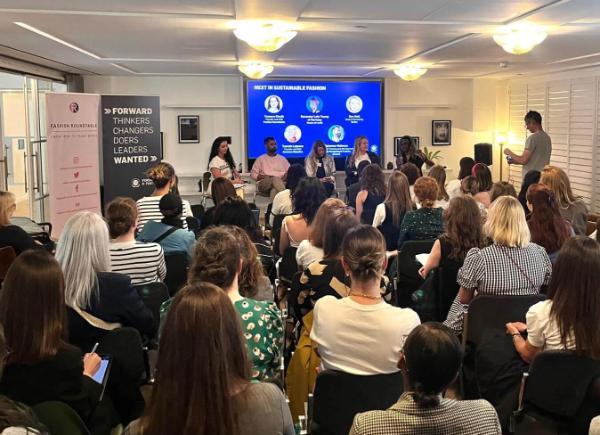 an audience watches a panel of people talking. There is screen behind them reading 'next in sustainable fashion'.