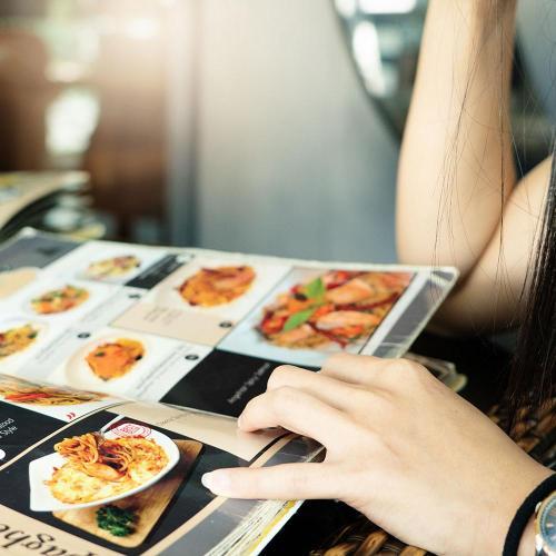 close up of person holding a food menu open. It includes photos of a variety of food and written information next to each.