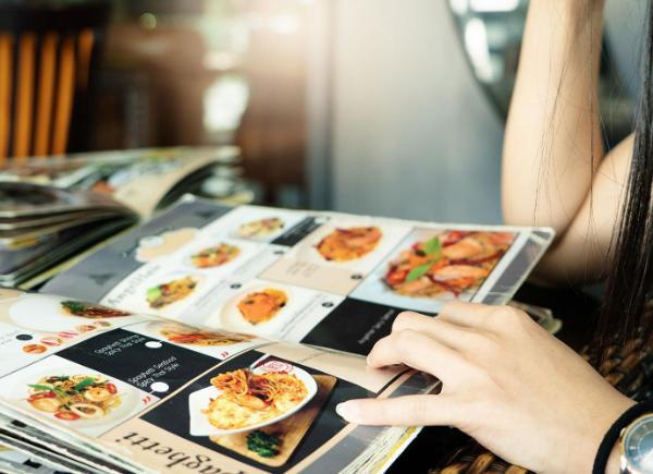 close up of person holding a food menu open. It includes photos of a variety of food and written information next to each.