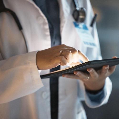 person in white coat with stethoscope around their neck using a tablet