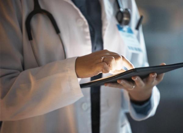 person in white coat with stethoscope around their neck using a tablet