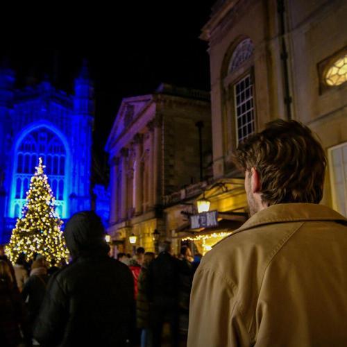 A man walks in front of the Abbey in Bath city centre at night, with the Christmas tree lights switched on