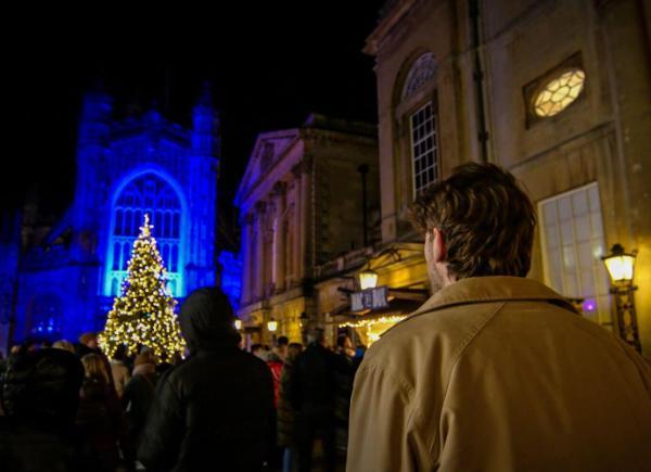 A man walks in front of the Abbey in Bath city centre at night, with the Christmas tree lights switched on