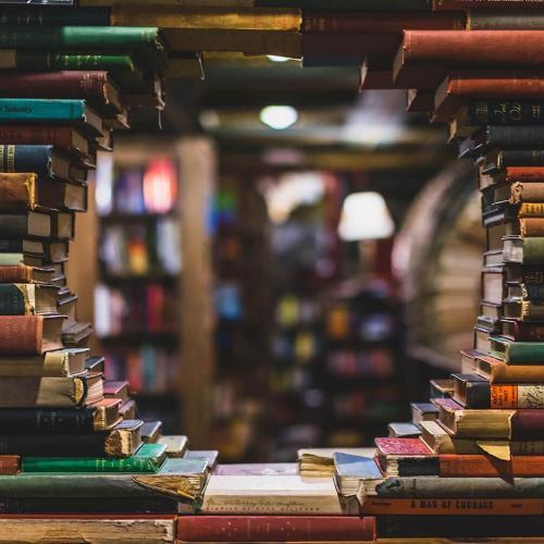 books stacked up, with a circular gap in them, revealing a room beyond the stack lined in bookshelves.