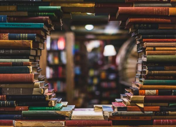 books stacked up, with a circular gap in them, revealing a room beyond the stack lined in bookshelves.