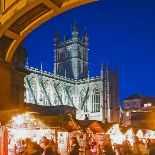 Bath Abbey at dusk surrounded by wooden Christmas Market huts