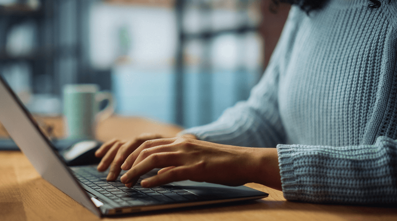 A woman sits at her desk typing on her laptop