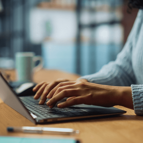 A woman sits at her desk typing on her laptop