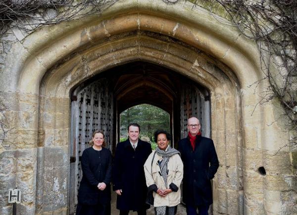 A group of four people stand under a stone archway and smile for a photo