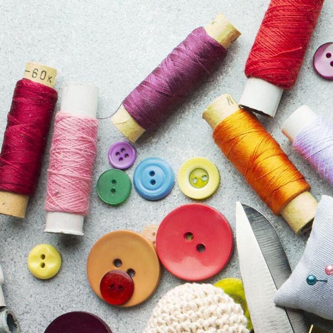 spools of thread, tape measure, scissors, a note pad, buttons and a pin cushion spread out on a white surface.