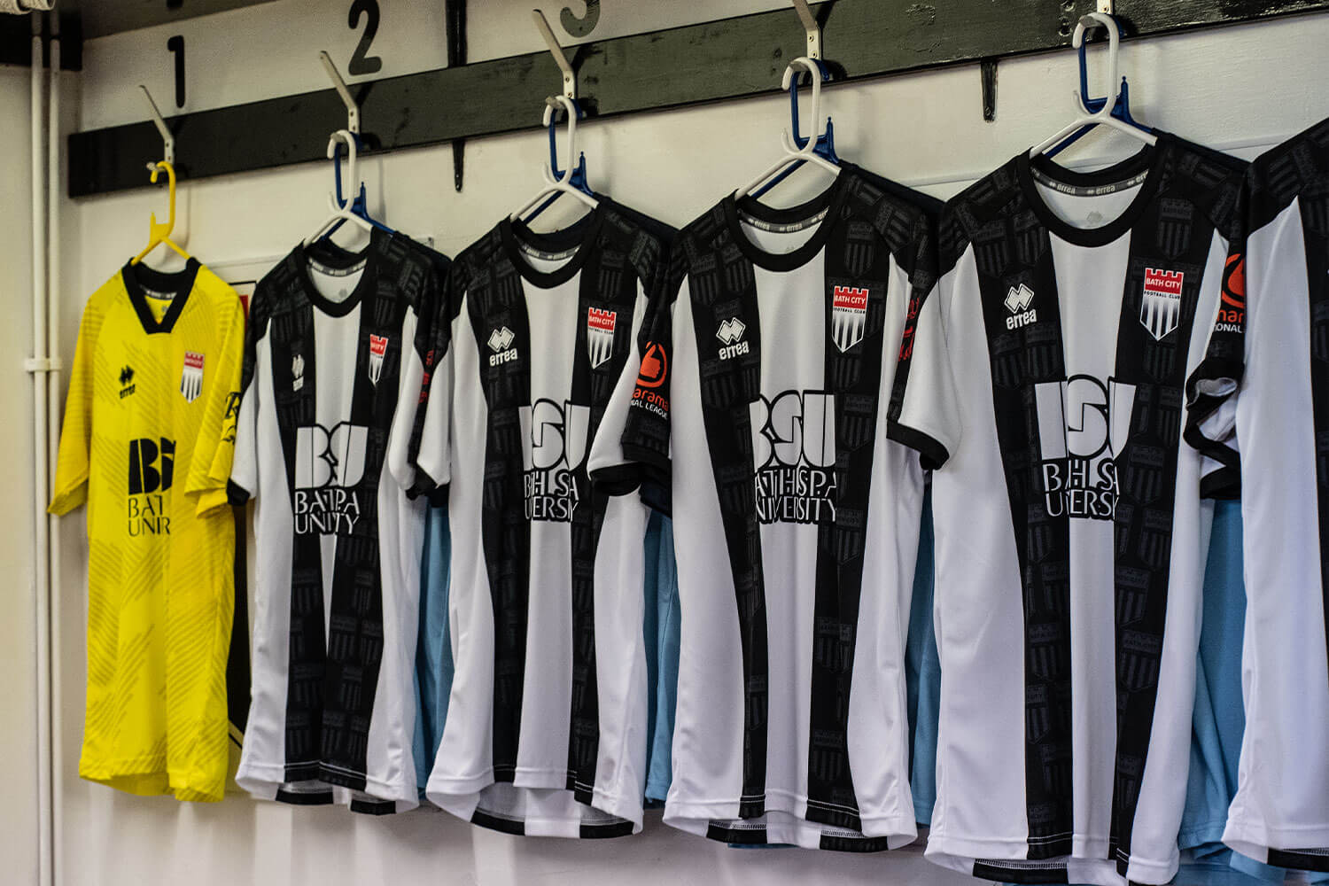 Bath City FC black and white shirts, showcasing the new BSU logo, hanging on clothing hangers in the home team dressing room