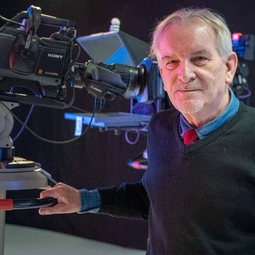 A man stood with his hand on a large television camera