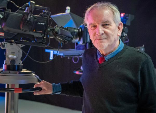 A man stood with his hand on a large television camera