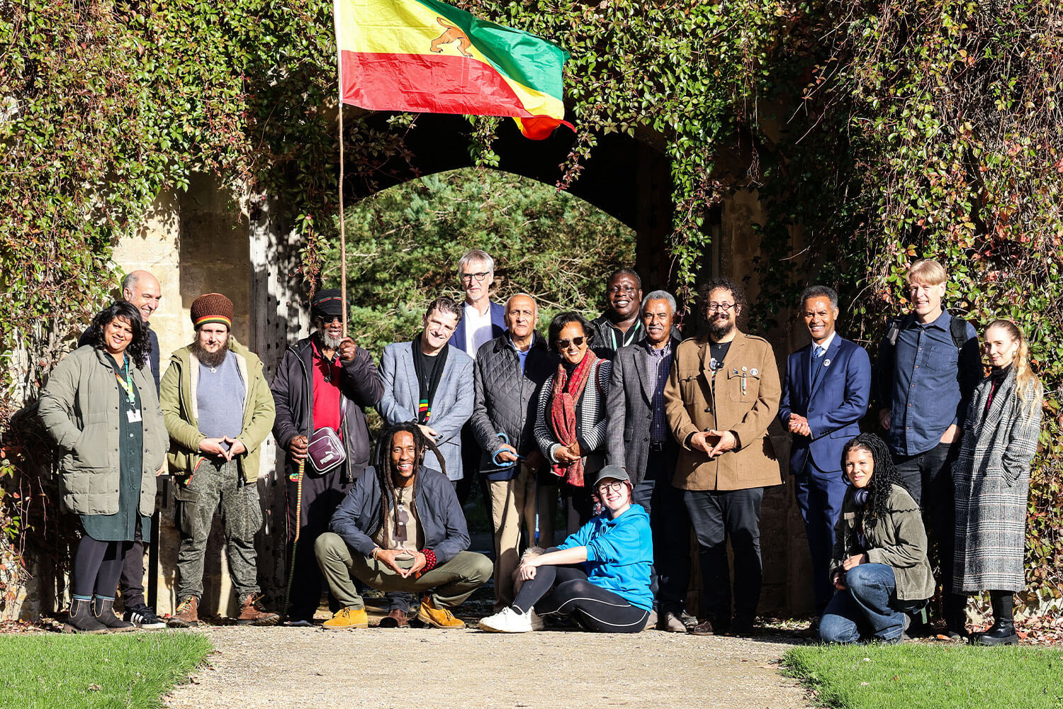 A large group of people stood in front of a leafy archway in the sunshine