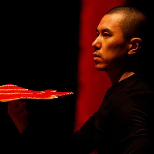 Dancer on stage under dark red lighting holding a fan