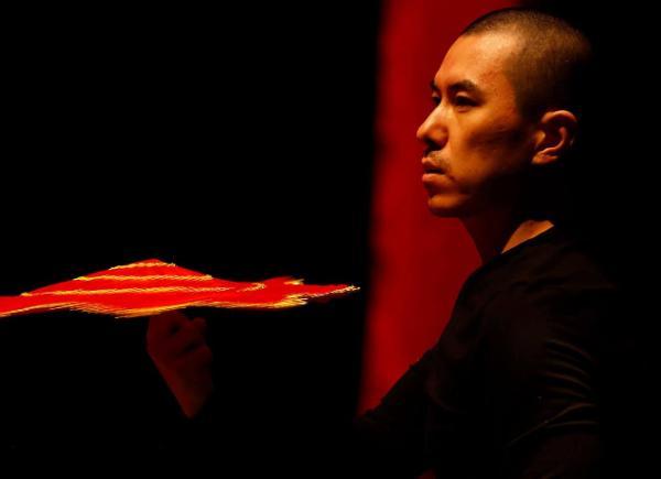 Dancer on stage under dark red lighting holding a fan