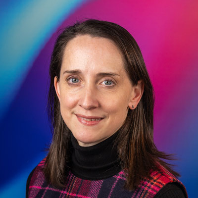 Person with long dark hair and tartan top smiling