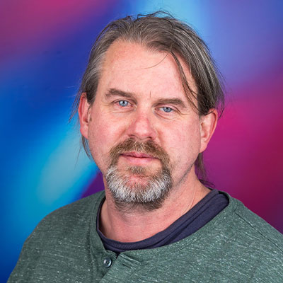 Headshot of person in green jumper with beard smiling