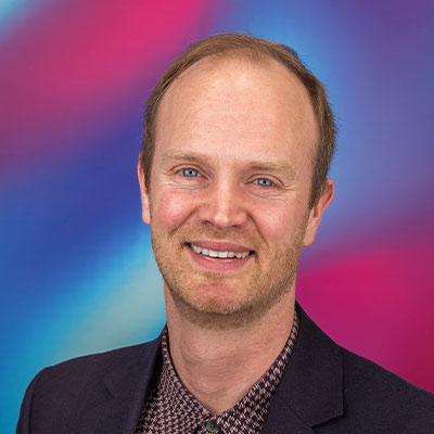 Headshot of person in herringbone shirt and dark jacket smiling