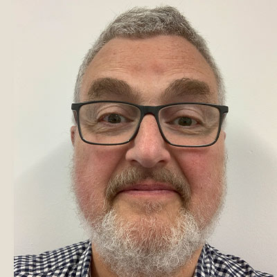 Person in checked shirt with white hair and beard and dark framed glasses