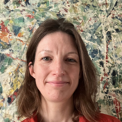 Person with light brown shoulder length hair in red shirt against abstract art