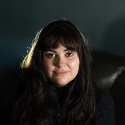 Person with long dark hair and fringe sitting on dark leather furniure