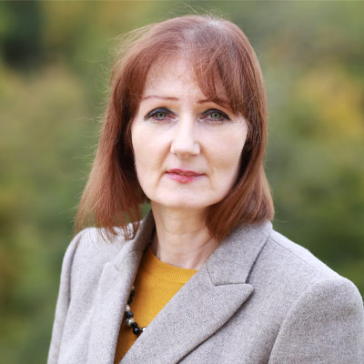 Person with shoulder length auburn hair in a light-coloured blazer and mustard top