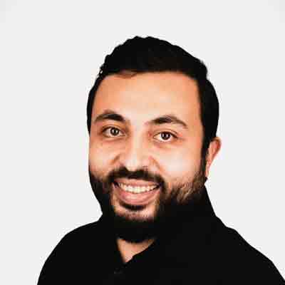 Person with short black hair and beard and moustache smiling in black shirt