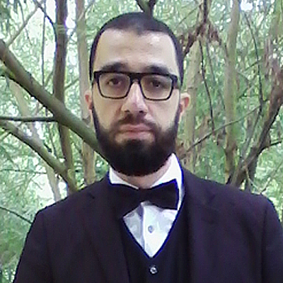 A person wearing a suit and black bow tie looks at the camera