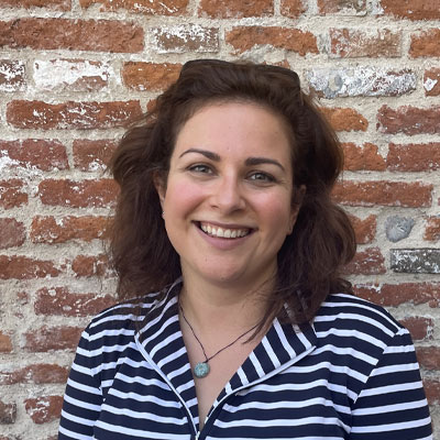 Person with long wavy dark hair in blue and white striped top in front of exposed brick wall