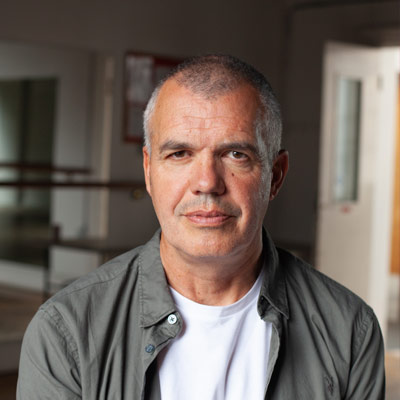 Person with short hair in white t shirt and grey shirt sitting in front of a doorway